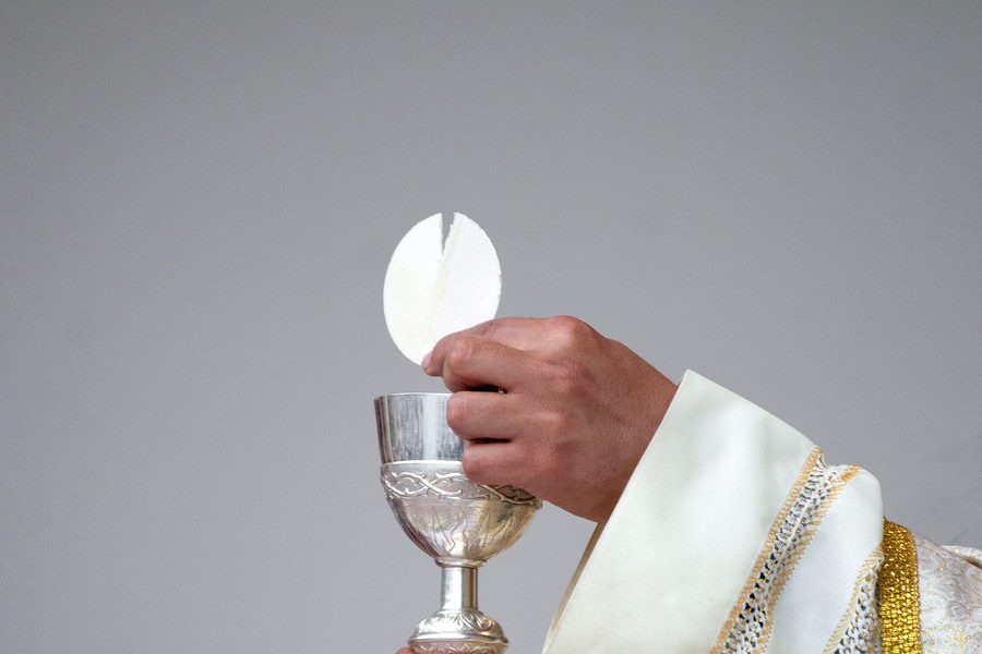 A priest holding a communion wafer above a silver chalice